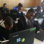 Students in a classroom working on Lenovo laptops while writing notes, demonstrating technology-supported learning and digital education in a school environment.