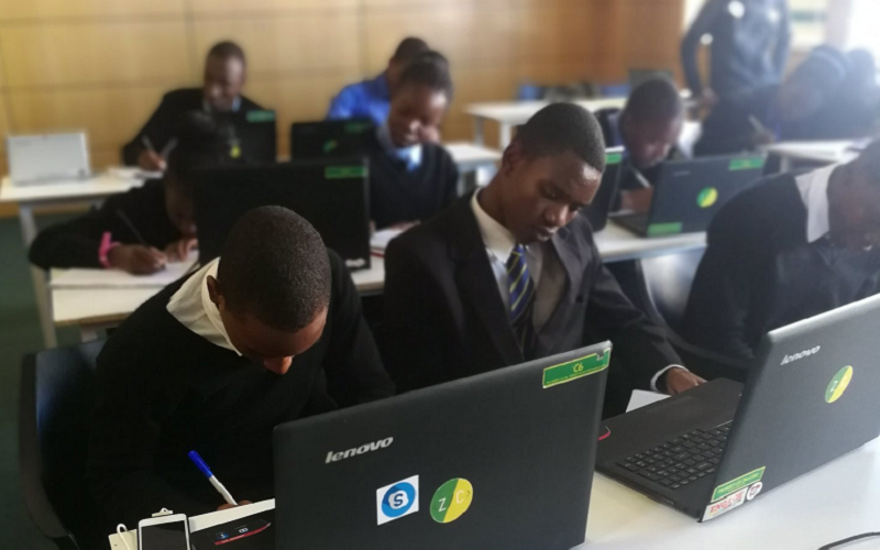 Students in a classroom working on Lenovo laptops while writing notes, demonstrating technology-supported learning and digital education in a school environment.