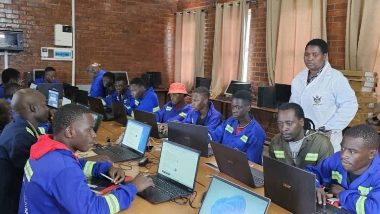 Young trainees working on laptops in a computer lab with an instructor supervising, illustrating technology training and digital skills development among youth.